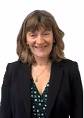 Smiling woman with shoulder-length brown hair wearing a black blazer over a green blouse with a white pattern.