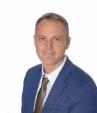 Portrait of a man in a blue suit jacket, white shirt, and patterned tie, set against a plain white background.