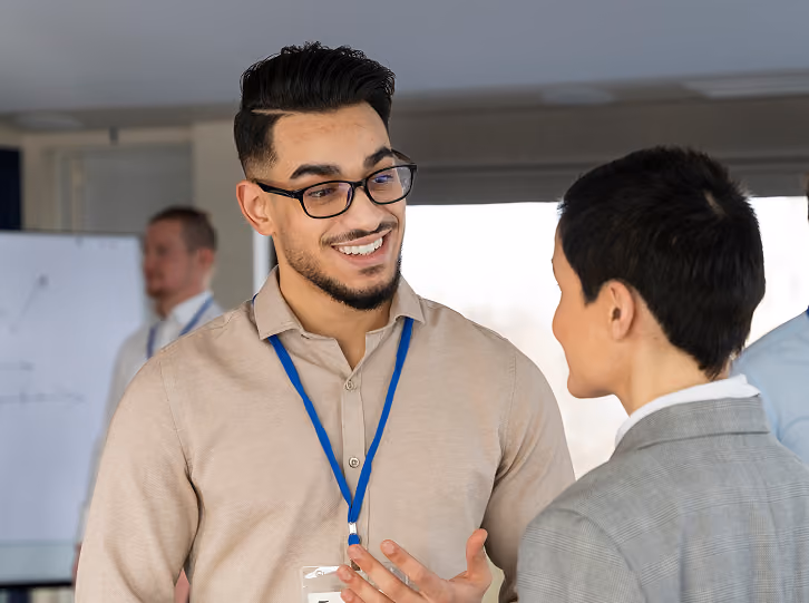 Two professionals wearing badges engage in conversation in a modern office setting.
