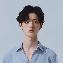 Portrait of a young man with wavy dark hair wearing a light blue button-up shirt against a plain light background.