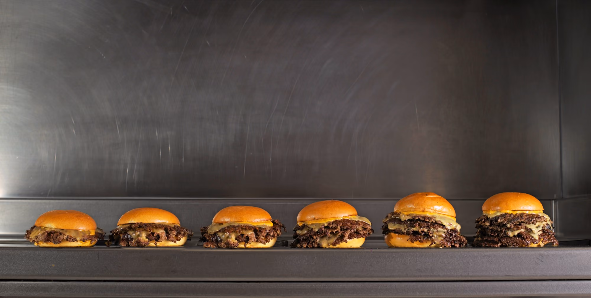 Six smash burgers alignés sur le grill, de 1 à 6 steaks