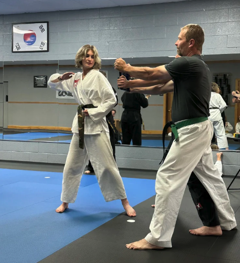 A karate instructor and student demonstrating a striking technique during a class on a blue training mat.