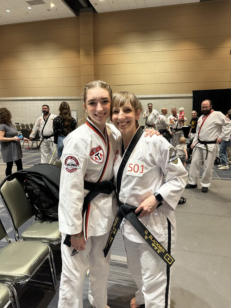Two smiling judokas in white gis and medals pose together at an indoor judo competition.