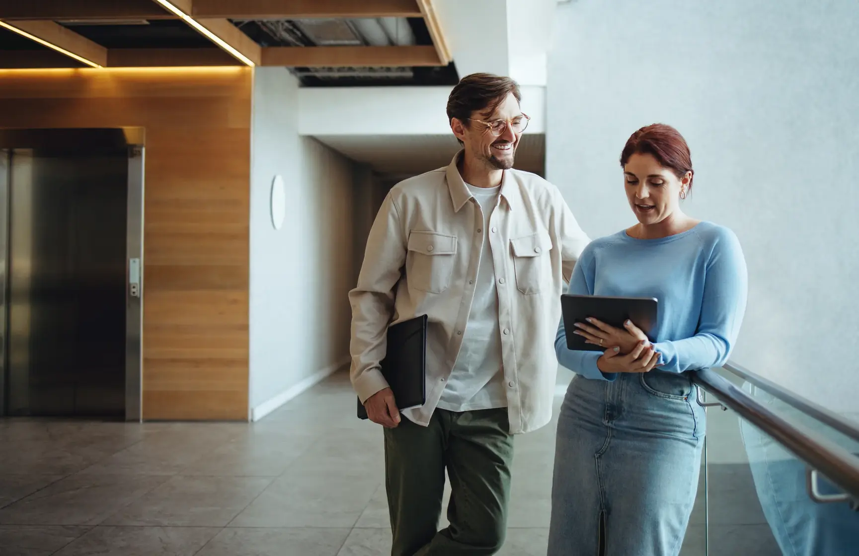 Two colleagues walking through an apartment lobby, one holding a tablet