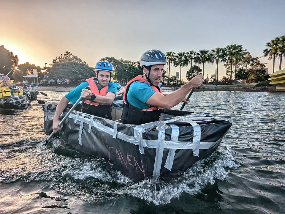 Two StrataMax team members paddling a cardboard boat in a team race