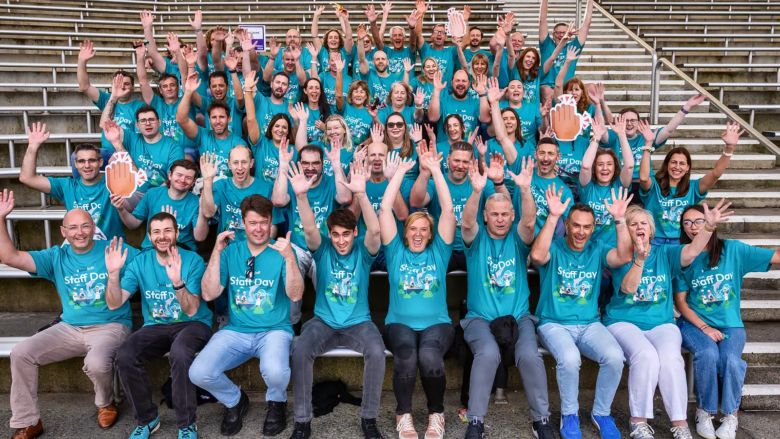 The StrataMax team in matching teal shirts, cheering on a grandstand at a staff day
