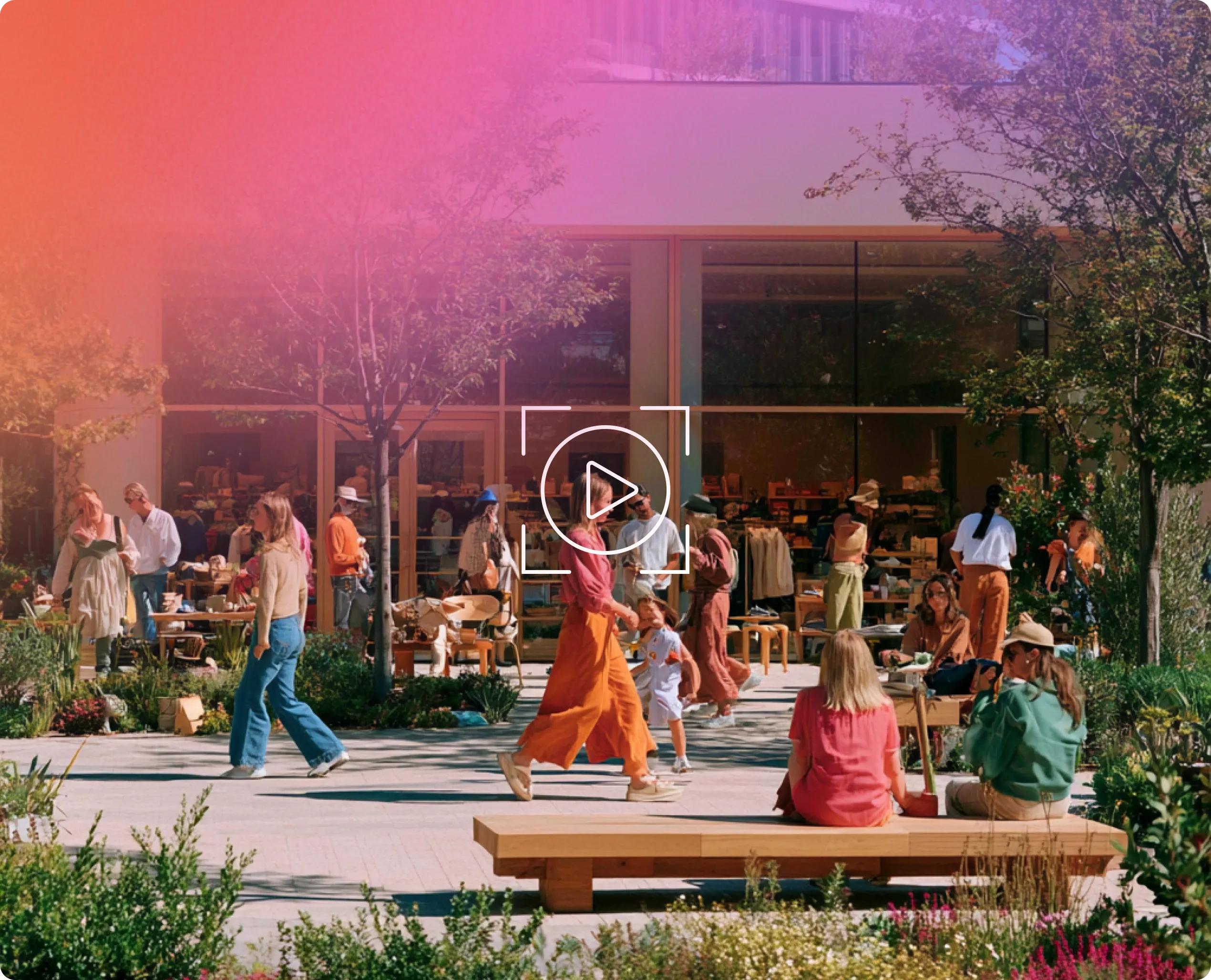 People walking and sitting near a retail store with greenery and trees outside on a sunny day.