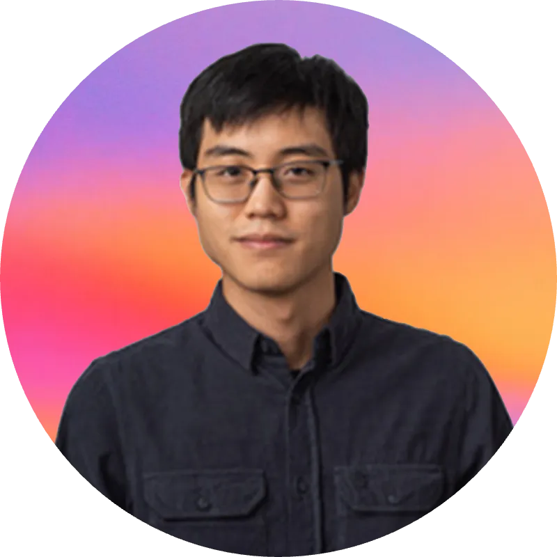 Portrait of a young man with black hair and glasses wearing a dark button-up shirt.
