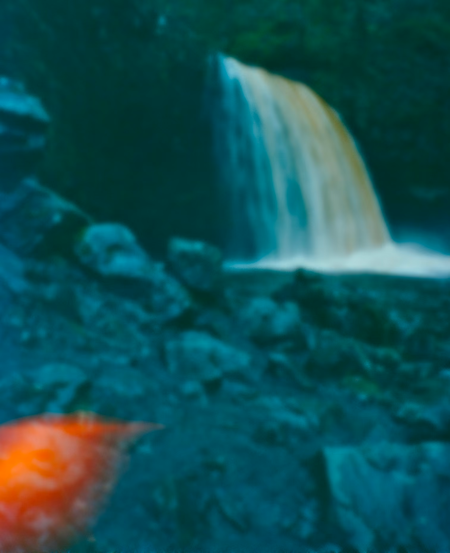 Blurry image of a waterfall with rocky terrain and a bright orange spot in the lower left corner.