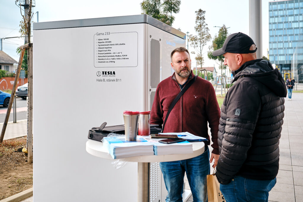 Rozhovor návštevníkov pri vonkajšom batériovom úložisku TESLA na Smart Energy Forum 2023