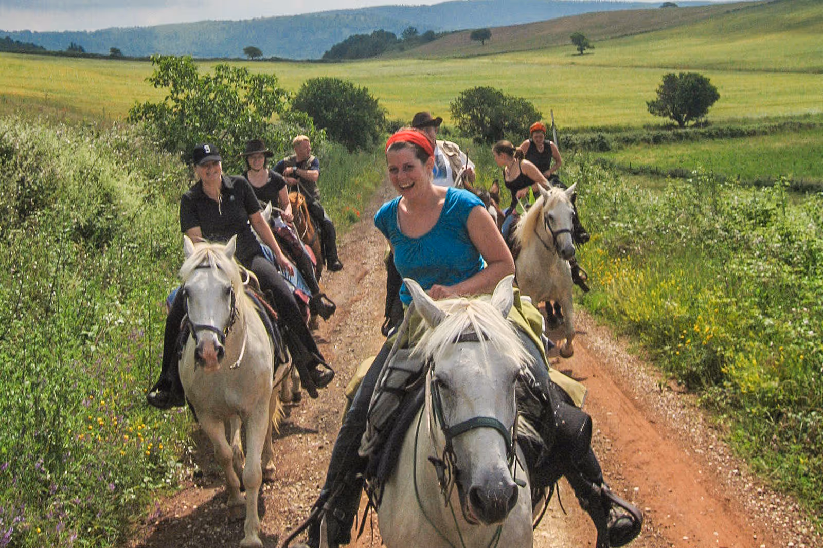 Un groupe de cavaliers joyeux avancent a allure rapide vers la caméra sur un chemin de campagne lors d'un séjour équestre en Toscane.