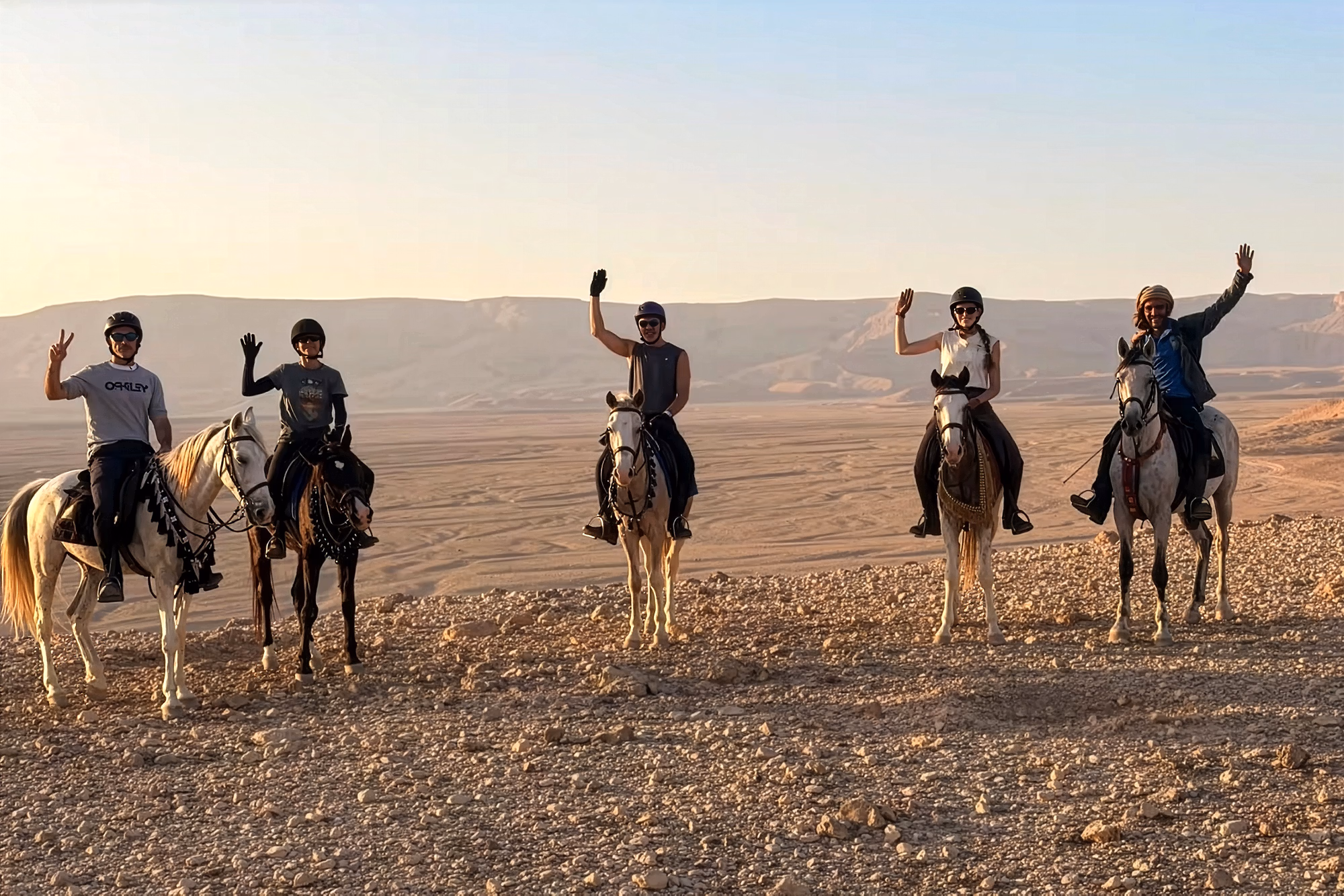 Quatre cavaliers et un guide local saluent l’objectif depuis une colline désertique lors d’une randonnée équestre en Égypte.