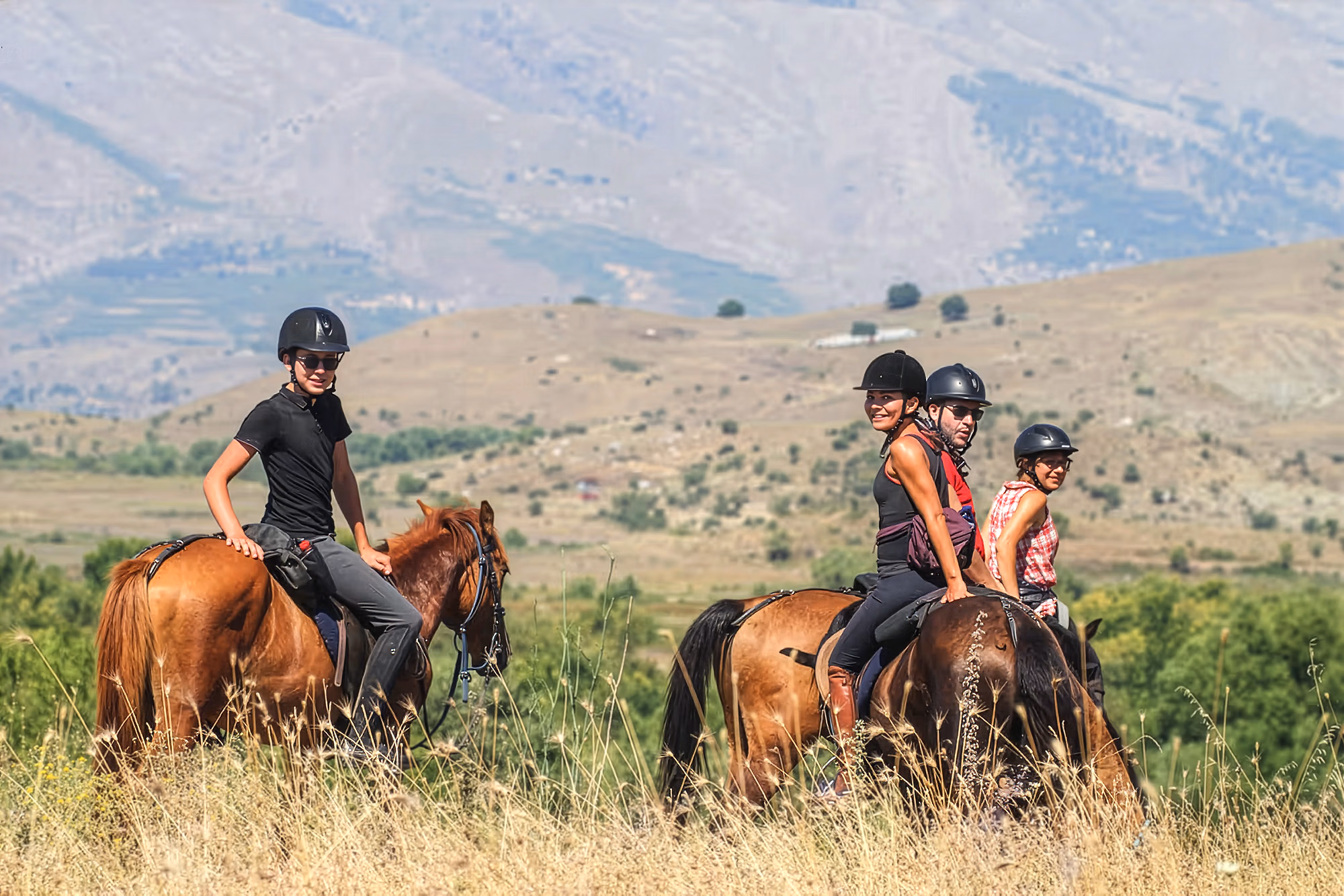 Quatre cavaliers se retournant vers l'objectif tout en traversant un plateau de montagne à cheval en Albanie.