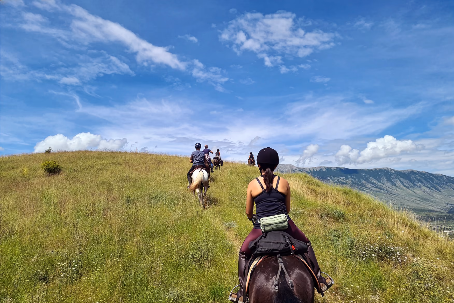 Groupe de cavaliers traversant une colline verdoyante avec les montagnes à l'horizon sous un ciel d'été parfaitement bleu lors d'une randonnée à cheval en Albanie.