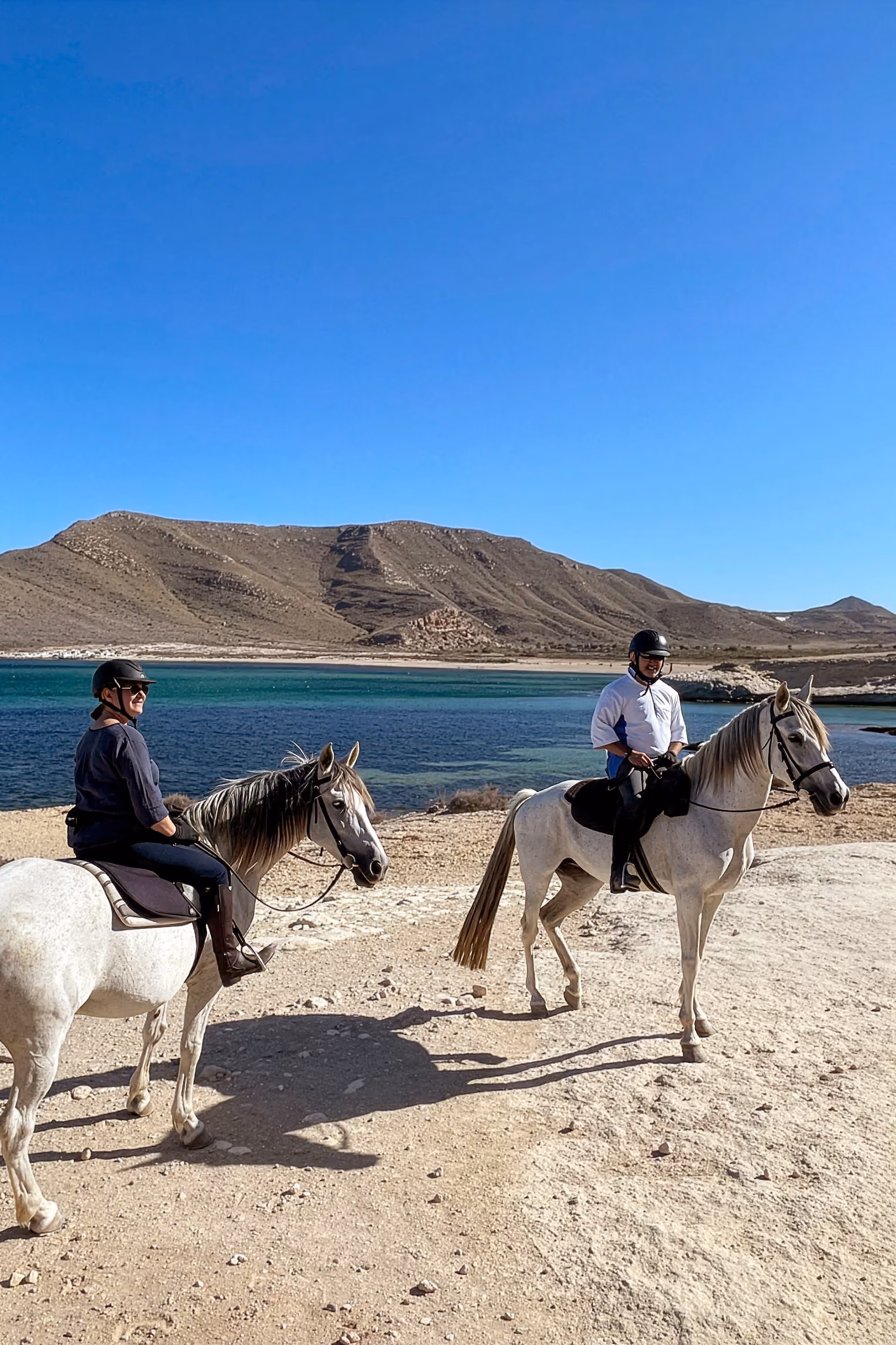 Deux cavaliers sur des chevaux blancs au bord d’une belle baie andalouse.