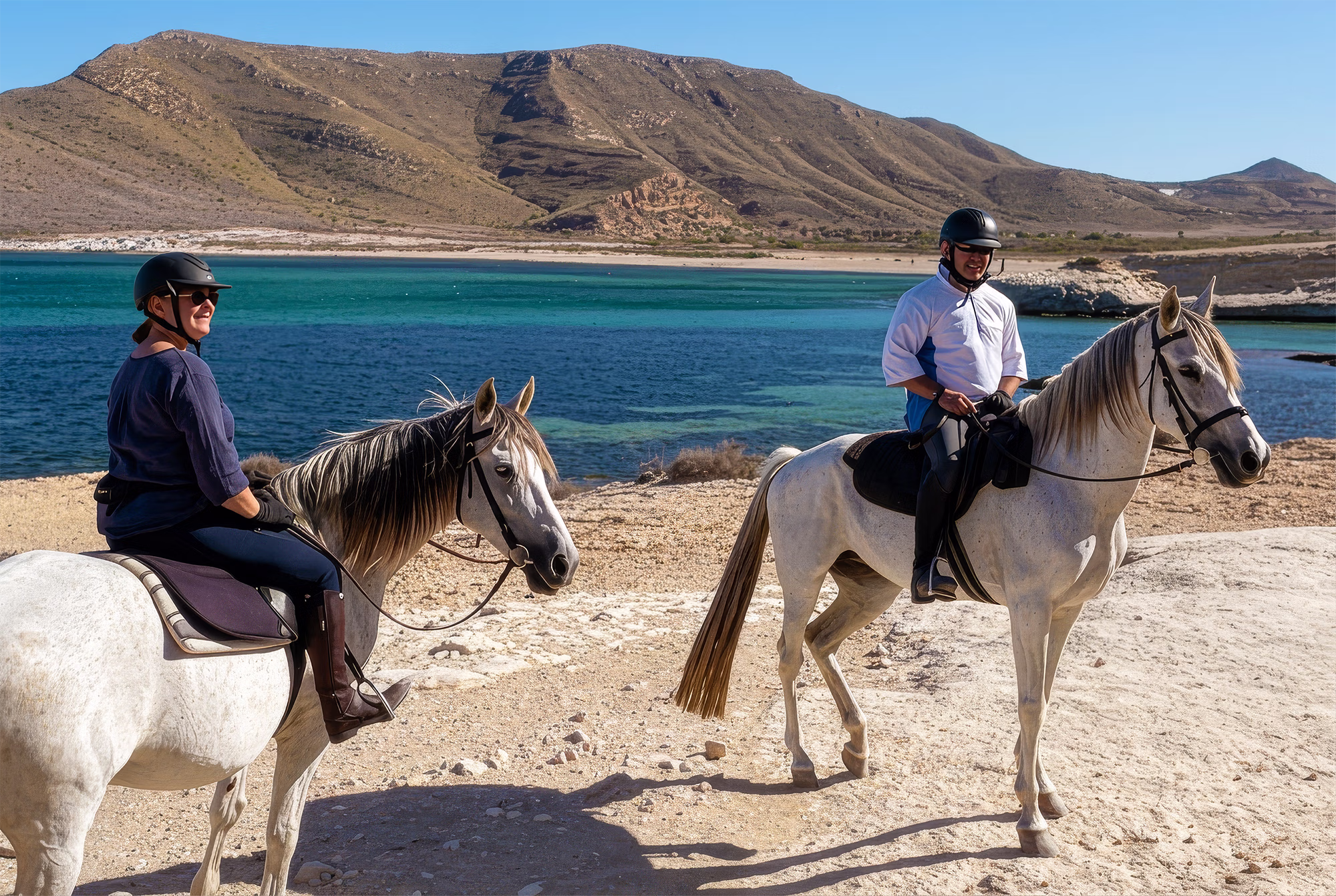 Un couple à cheval contemple le paysage, avec une baie et les collines de Cabo de Gata en arrière-plan.