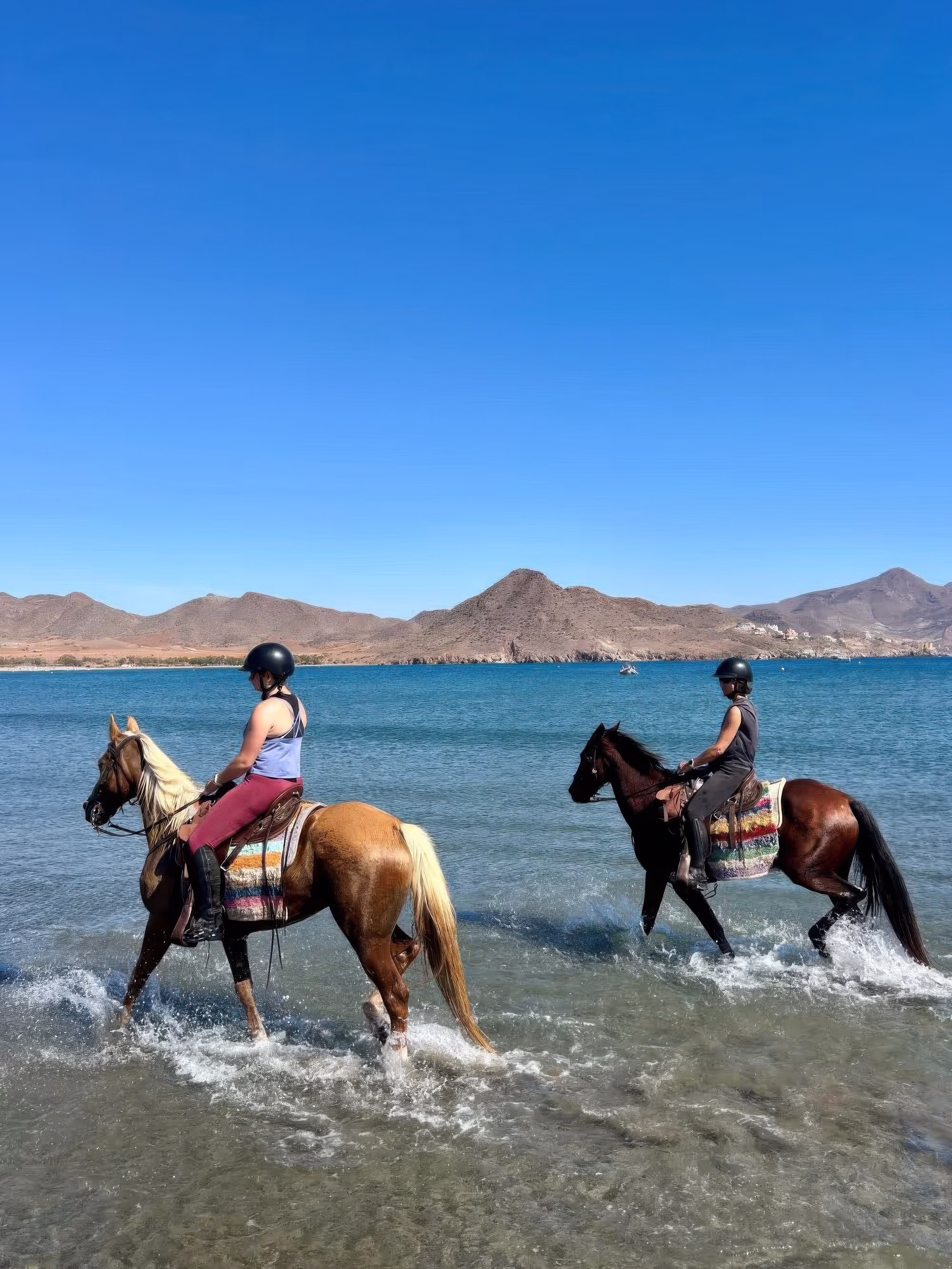 Deux cavaliers traversent la mer à cheval par une journée ensoleillée lors d’une randonnée équestre à Cabo de Gata.