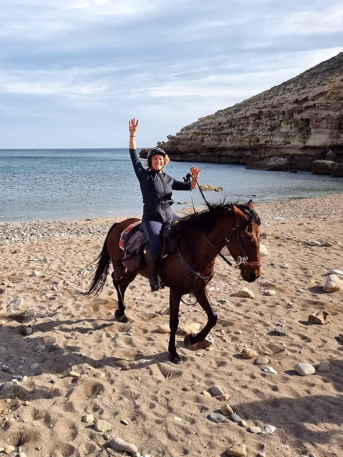 Un cavalier souriant salue l’objectif à cheval sur la plage.