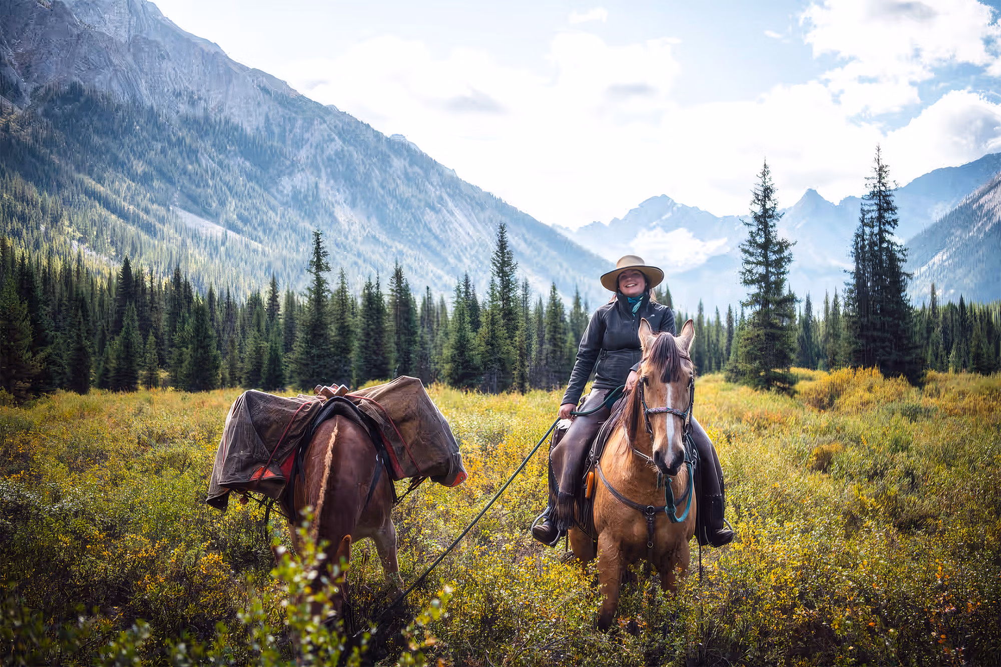 Une guide à cheval traverse la végétation de montagne tout en menant un cheval de bât.