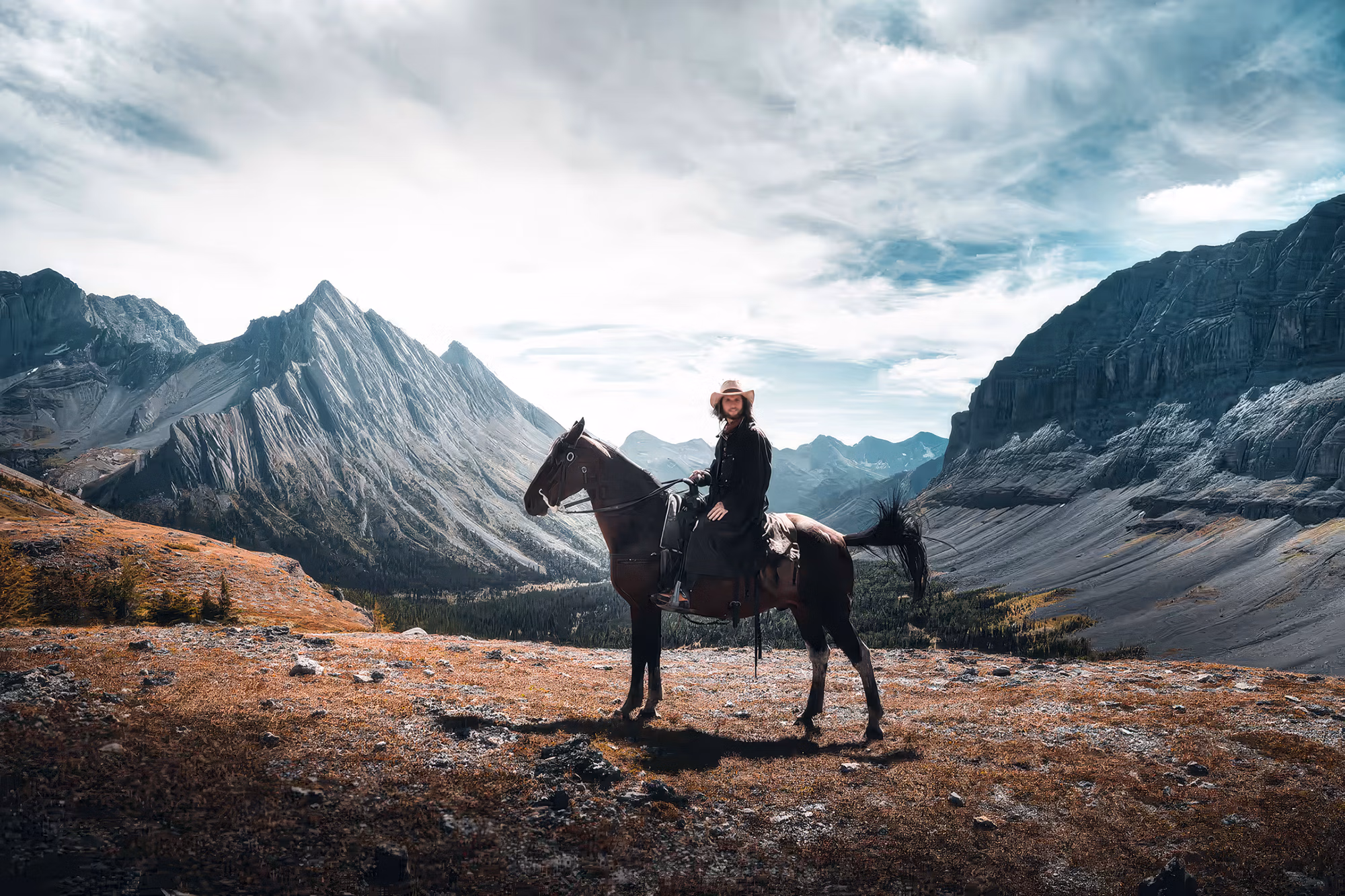 Un cheval attentif, oreilles dressées, et son cavalier posant devant le spectaculaire paysage des Rocheuses canadiennes.