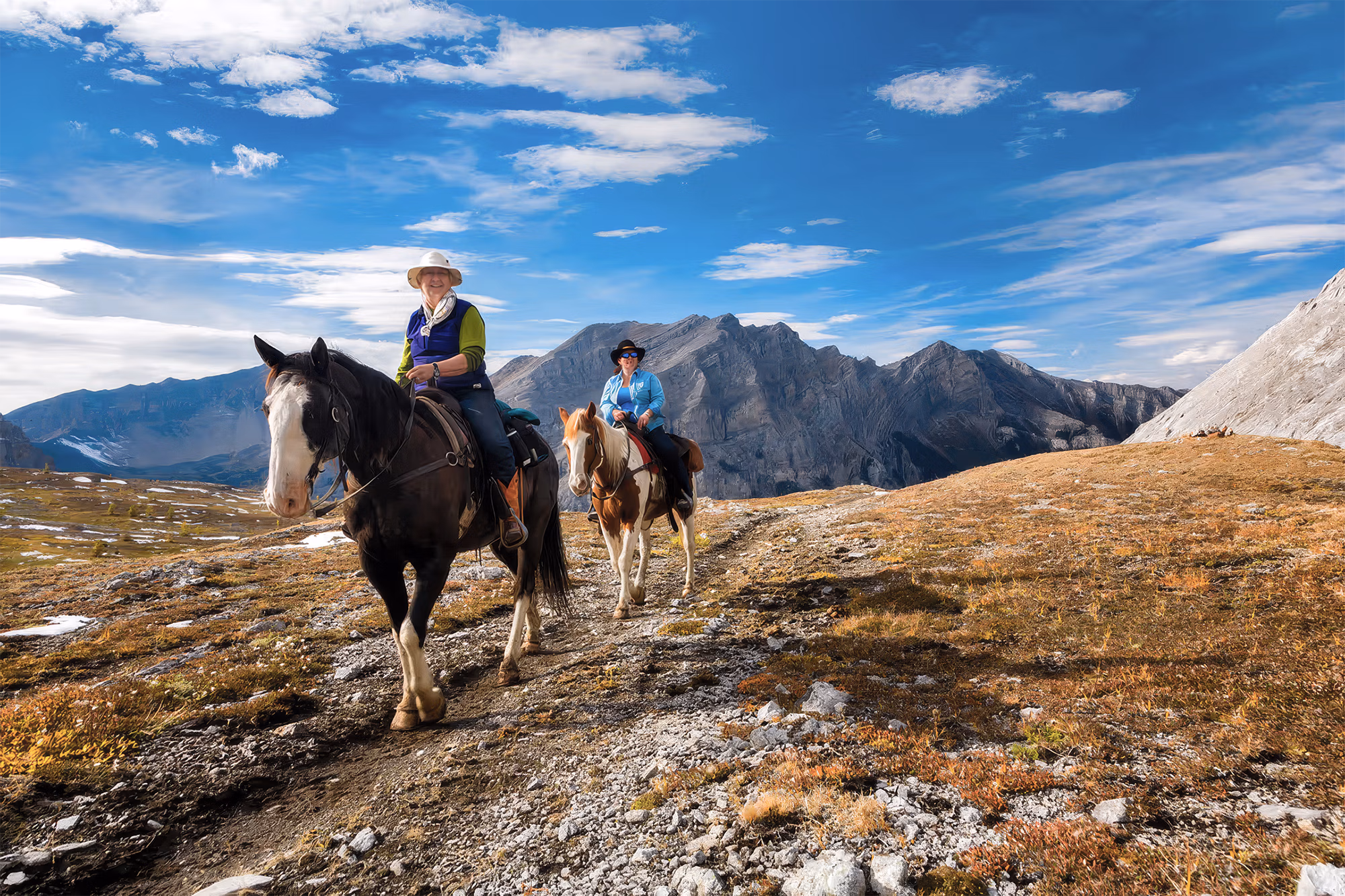 Deux cavaliers à cheval franchissant un col de haute montagne dans les Rocheuses canadiennes.