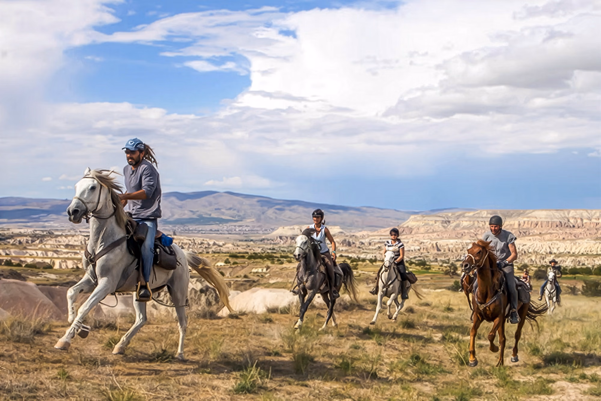 Un groupe de cavaliers galope à travers les paysages de Cappadoce, avec les célèbres formations rocheuses volcaniques en arrière-plan.
