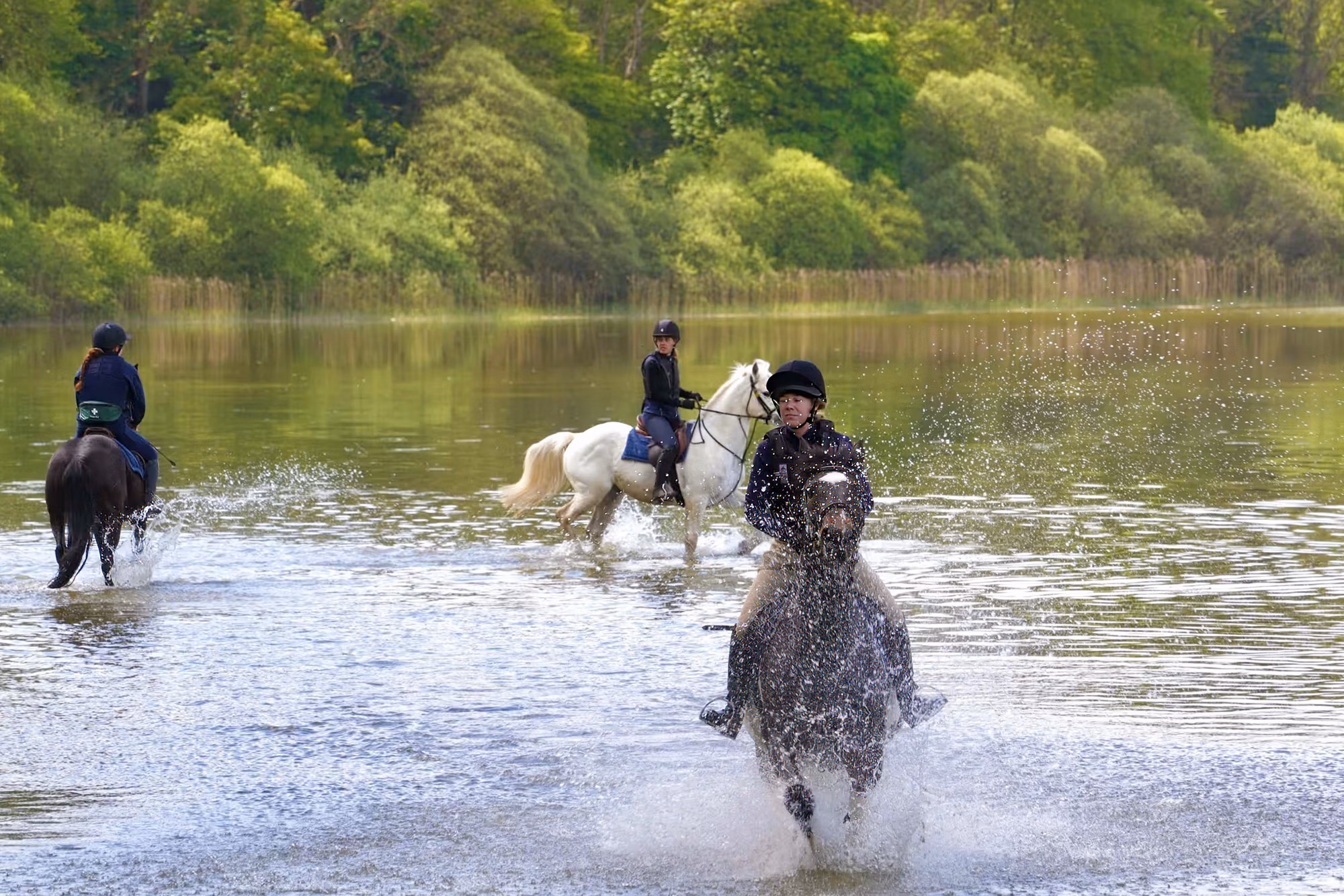 Un groupe de cavaliers traversant un lac lors d’un séjour équestre à Castle Leslie en Irlande.