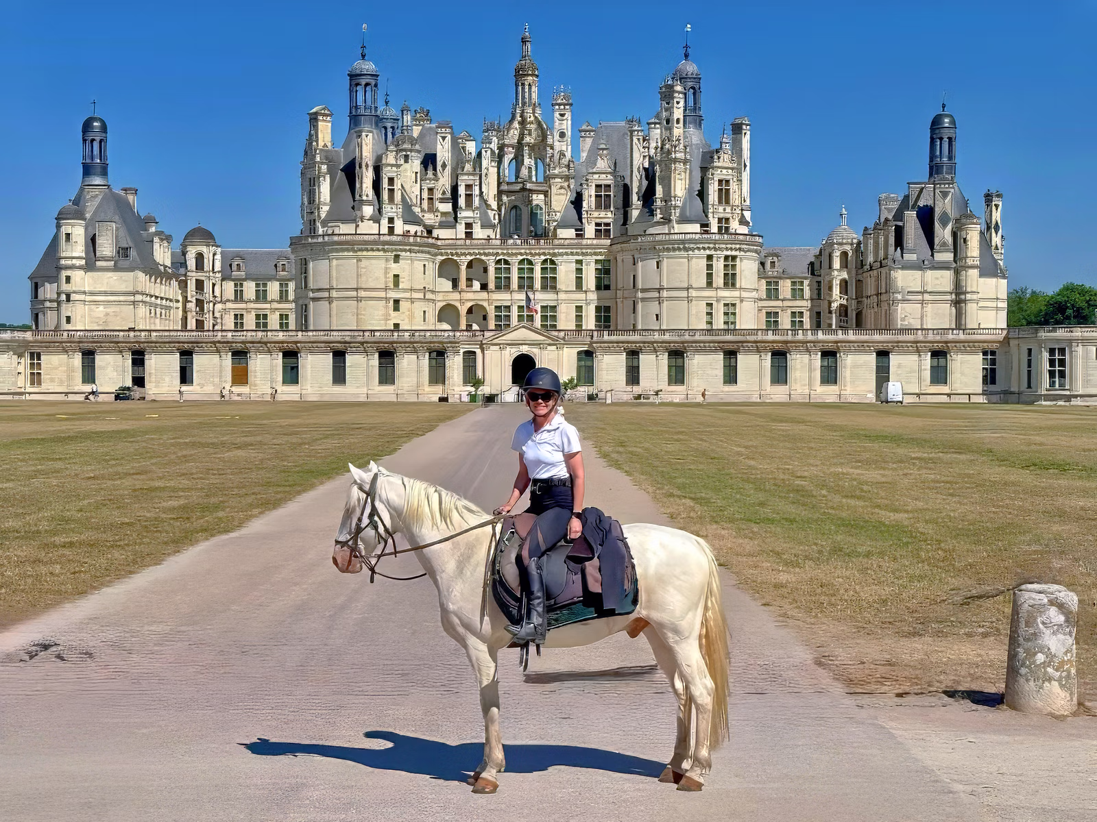 Une cavaliere souriante posant a cheval devant un majestueux Chateau de la Renaissance lors d'un séjour équestre en France
