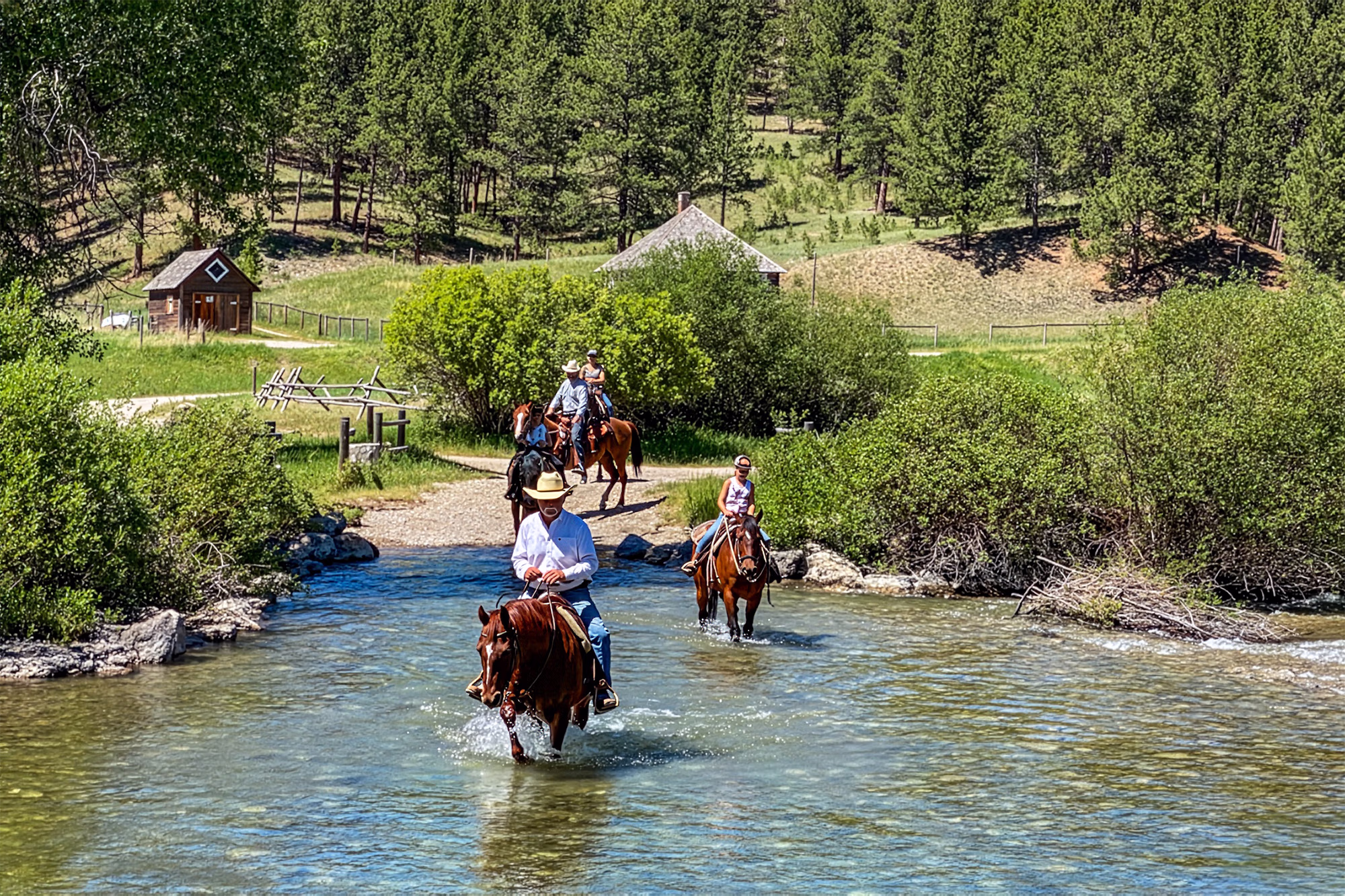 Cavaliers et chevaux traversant une rivière lors d’un séjour équestre au Circle Bar Ranch.