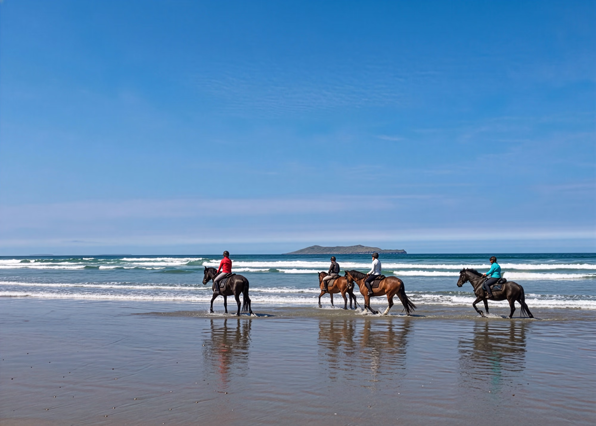 Quatre cavaliers avancent en file le long du rivage, au bord de petites vagues.