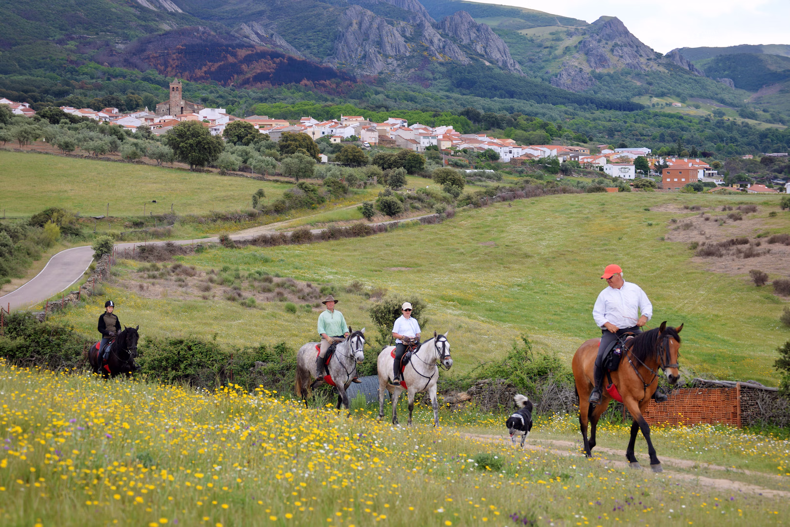 Des cavaliers et leur guide progressent sur un chemin s'éloignant d'un village lors d'une randonnée équestre en Espagne.