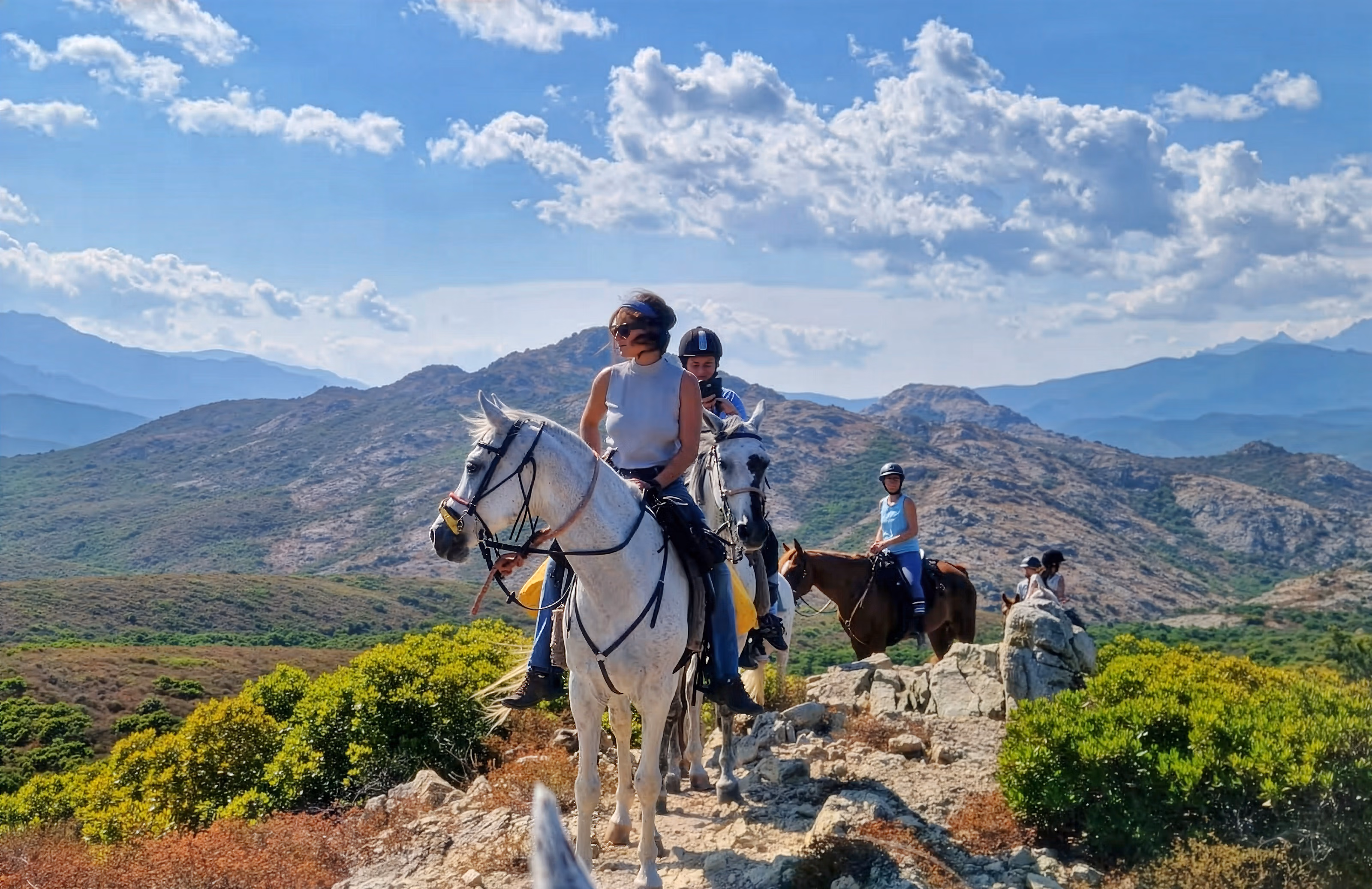 Groupe de cavalieres a cheval au sommet d'une crete montagneuse en Corse admirant le paysage.
