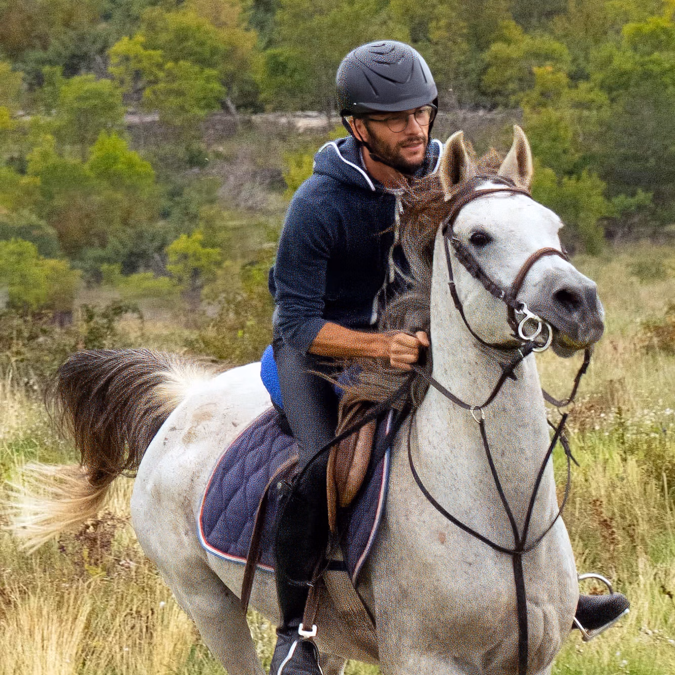 Un cavalier galope sur un cheval blanc à travers une vaste campagne ouverte.