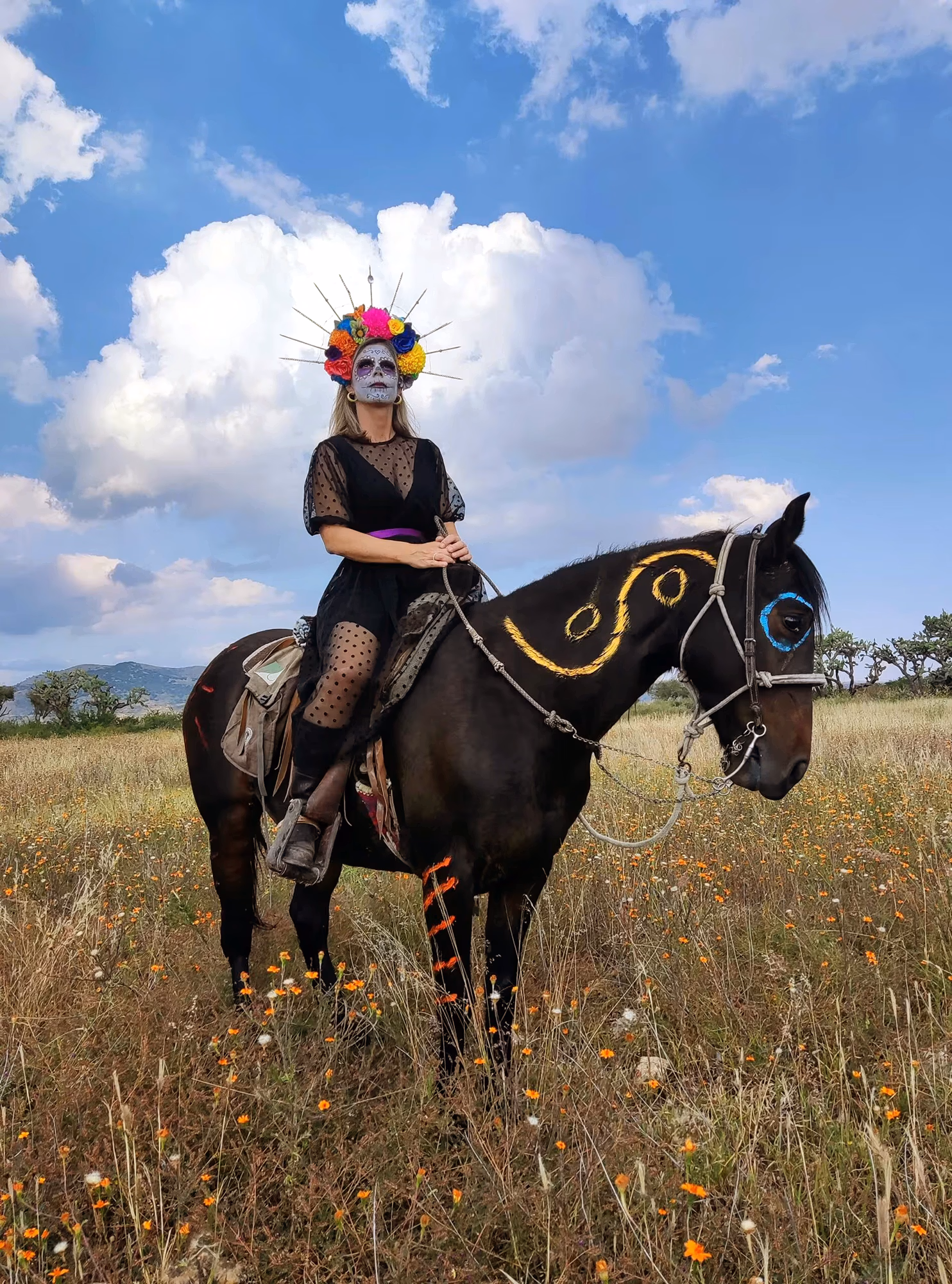 Une cavalière avec un maquillage traditionnel du Día de los Muertos sur un cheval décoré de motifs assortis.