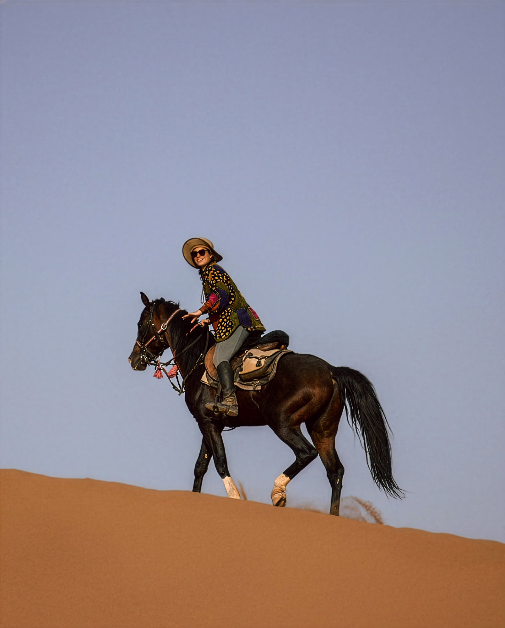 Un cavalier solitaire gravit une dune de sable à cheval.