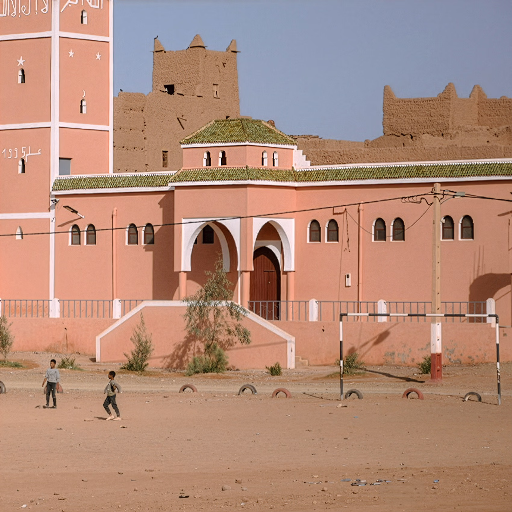 Des enfants jouent au football sur un terrain poussiéreux dans une ville du désert marocain.