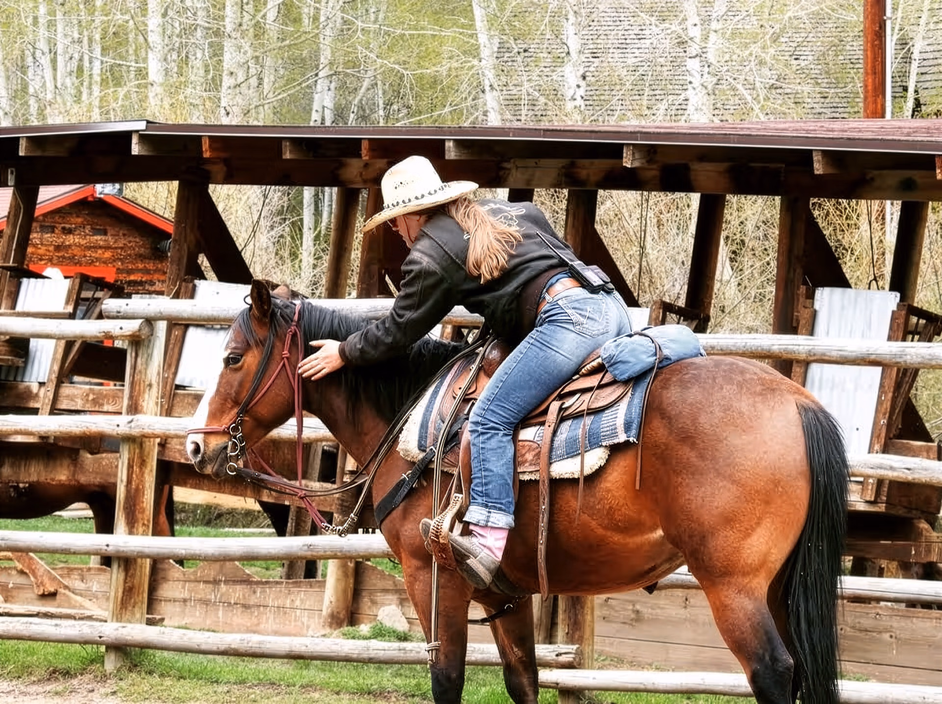 Une femme en tenue de cowboy caresse l'encolure de son cheval dans un ring d'entrainement Western