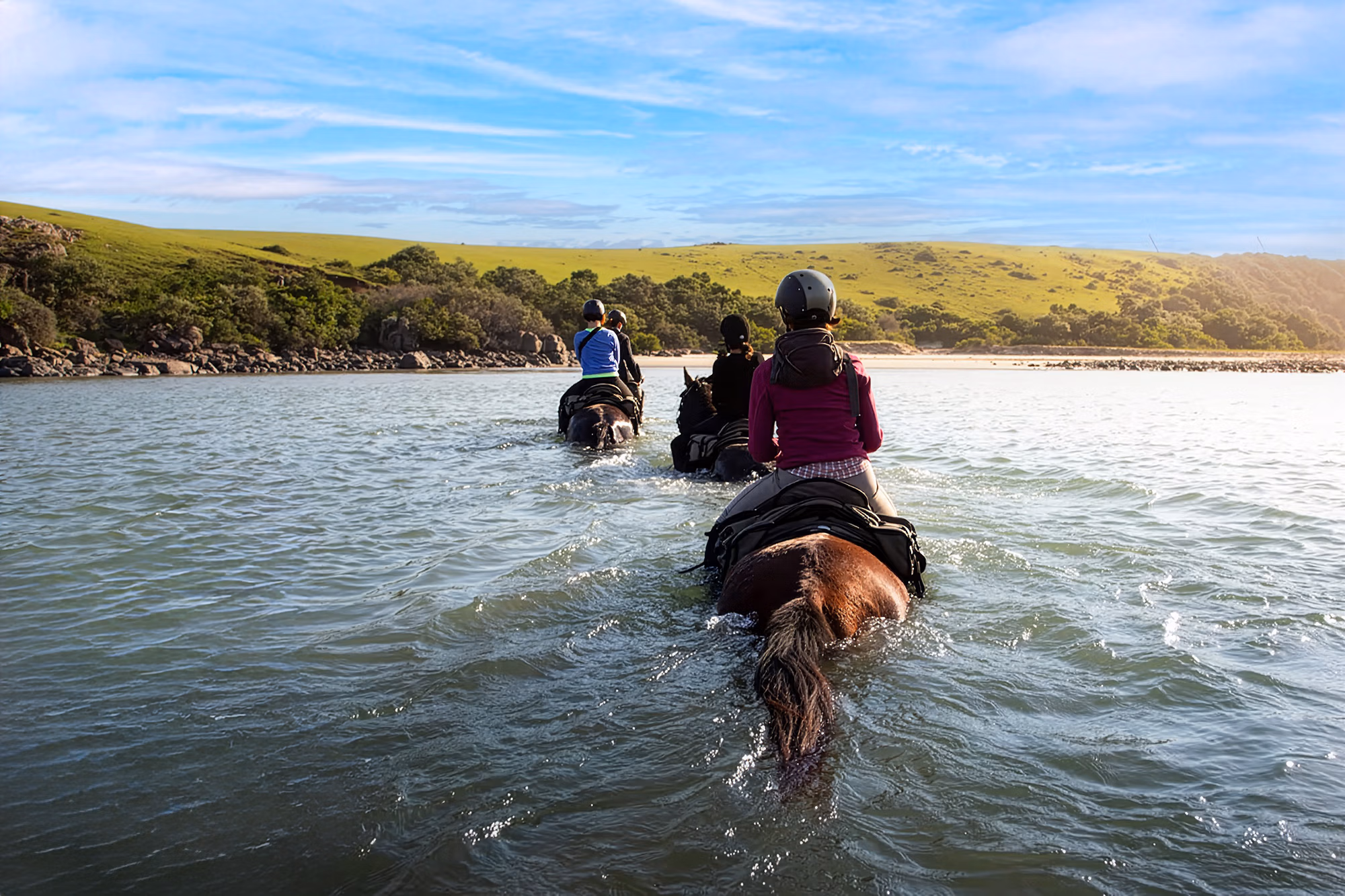 Trois cavaliers traversent une étendue d’eau profonde avec leurs chevaux.