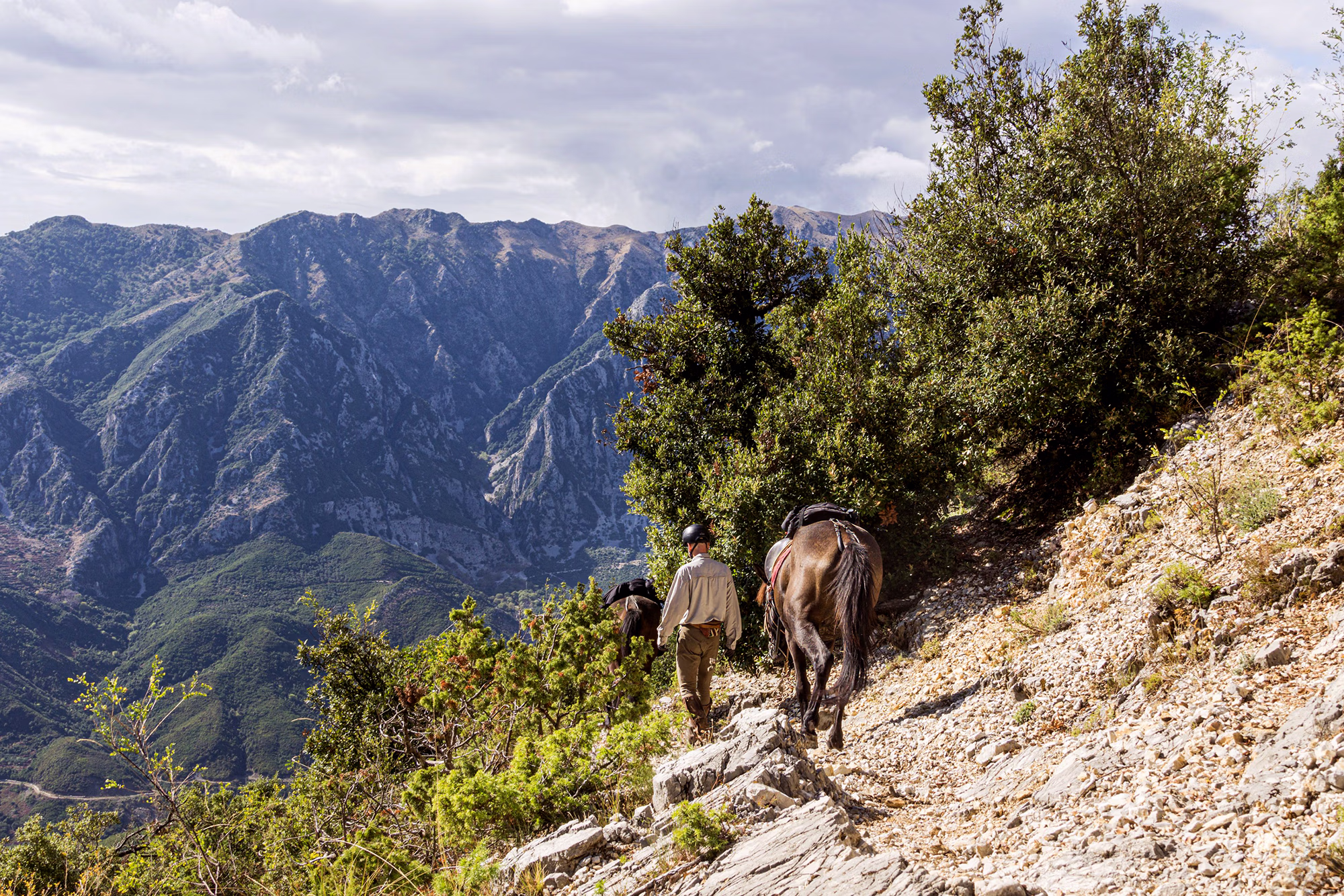 Un homme à pied mène son cheval le long d'un sentier de montagne escarpé et rocailleux, en empruntant le mythique et exigeant Sentier de Skerdilajdi en Albanie.
