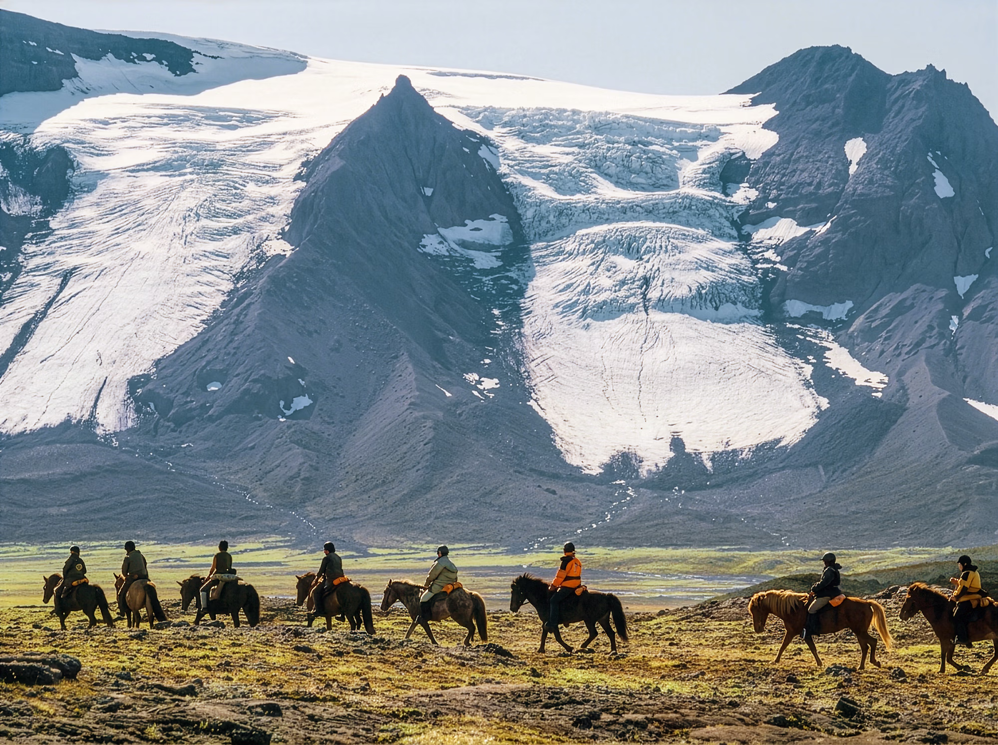 Un groupe de cavaliers traverse les Hautes Terres volcaniques et désertiques d’Islande, avec un immense glacier en arrière-plan.