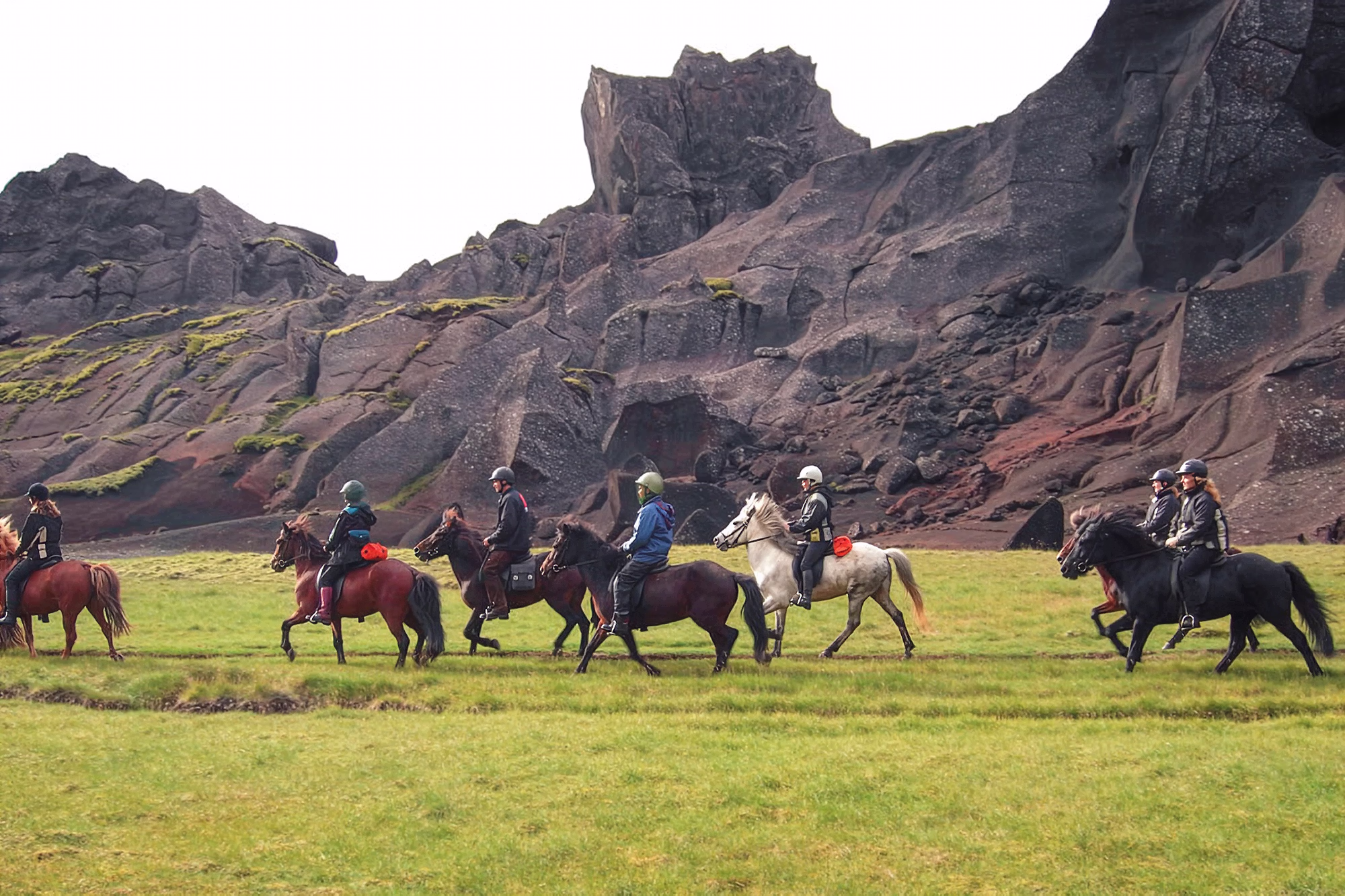Cavaliers traversant à cheval un paysage de formations volcaniques escarpées sur de l'herbe verte sur la Route de Kjölur en Islande.