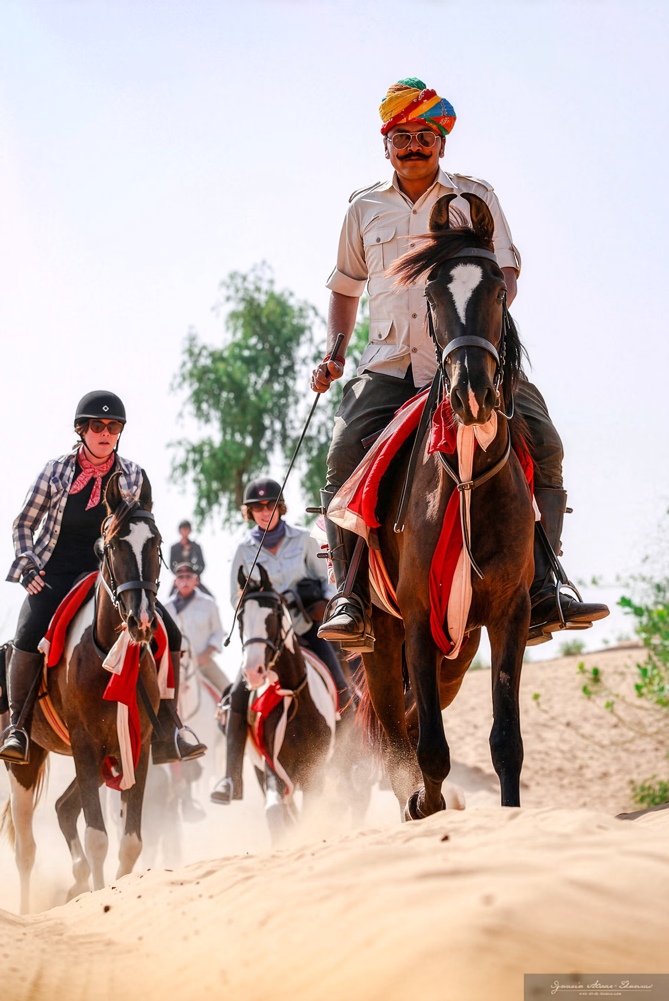 Un guide local portant un turban traditionnel ouvre la marche à cheval.