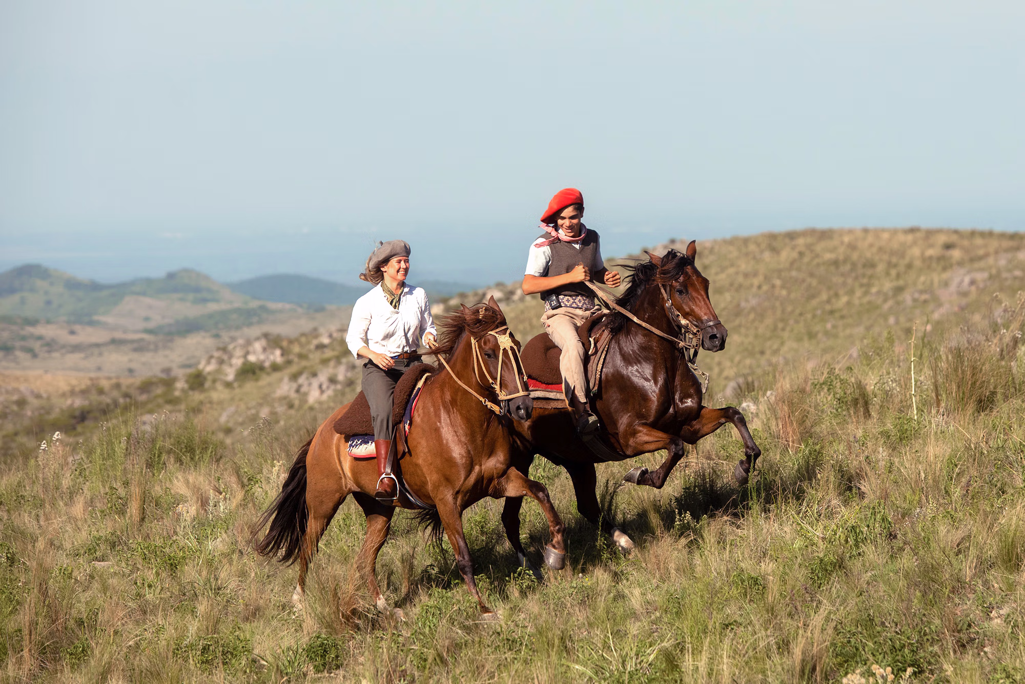 Deux gauchos argentins portant des chapeaux traditionnels montent à cheval côte à côte sur une colline en pente douce.