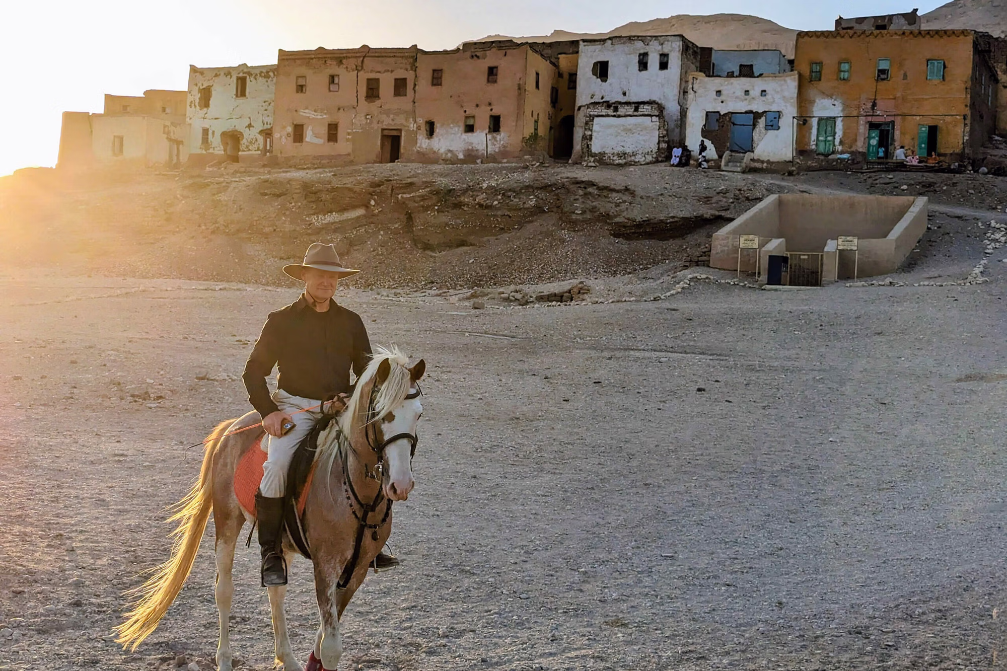 Un cavalier se détache dans la lumière du coucher du soleil, devant des bâtiments traditionnels en briques de terre.