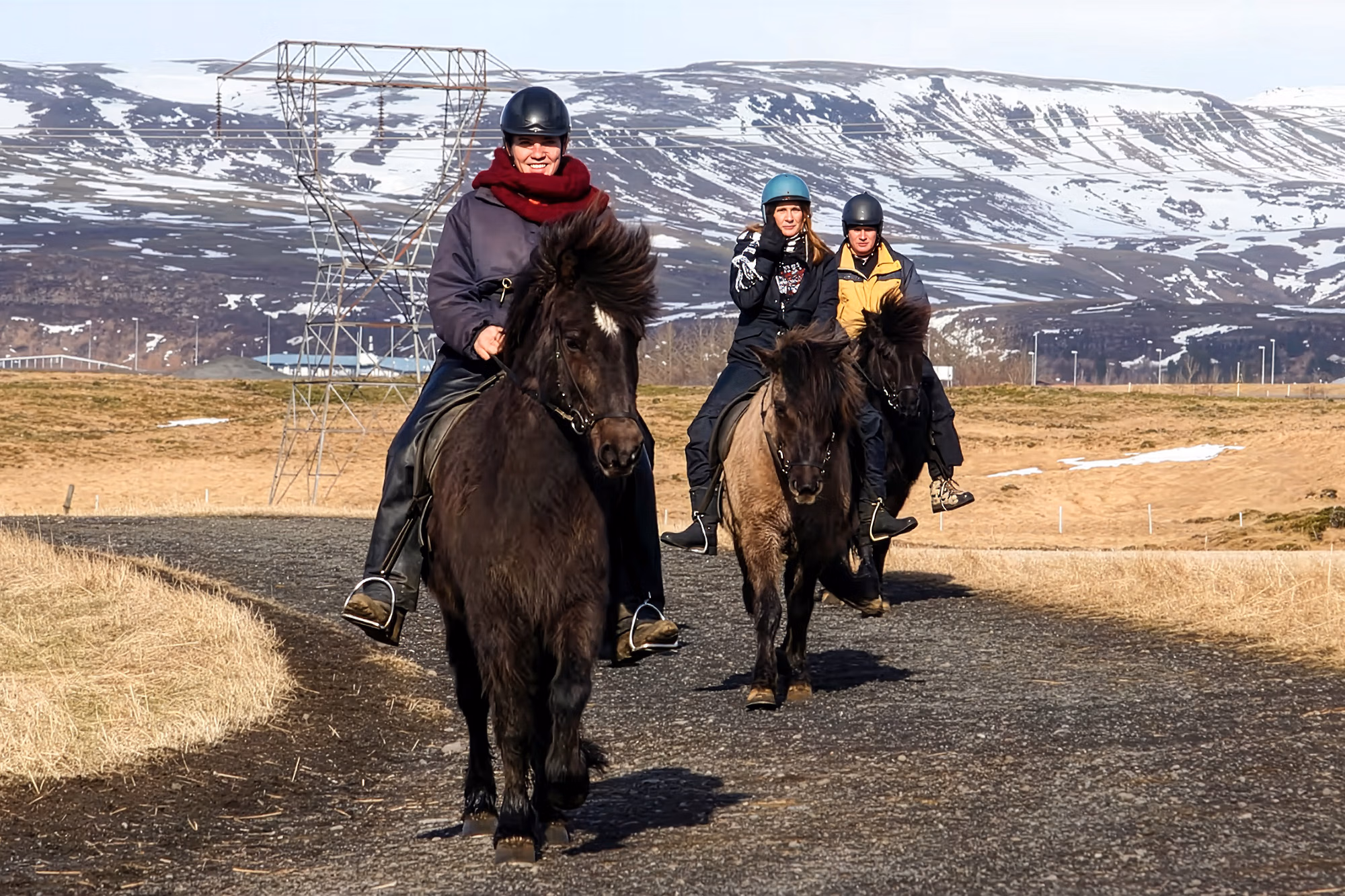 Cavaliers sur des chevaux islandais avançant sur un chemin accidenté devant une colline enneigée lors d’un voyage à cheval en Islande.