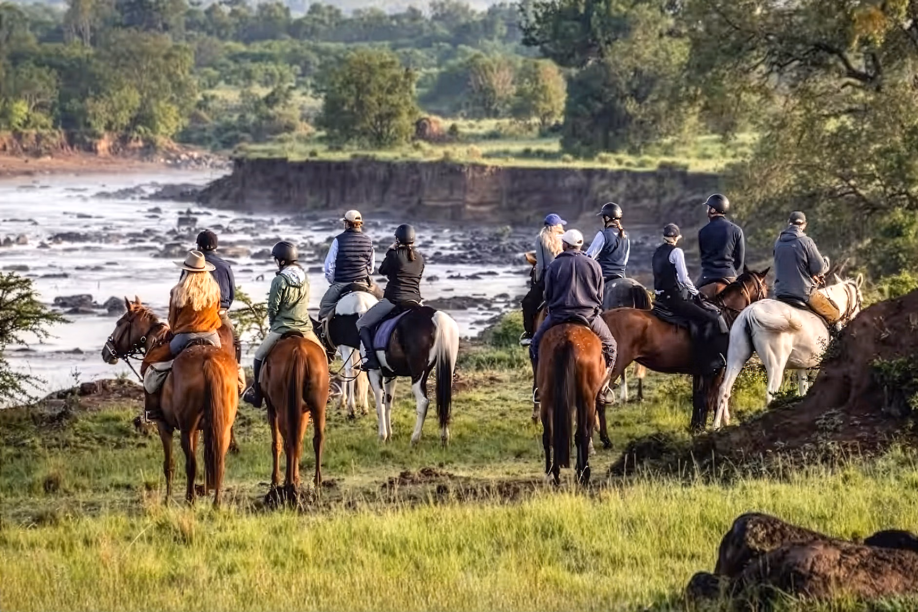 Un groupe de cavaliers sur une crête herbeuse observe une rivière au loin lors d’un safari équestre.