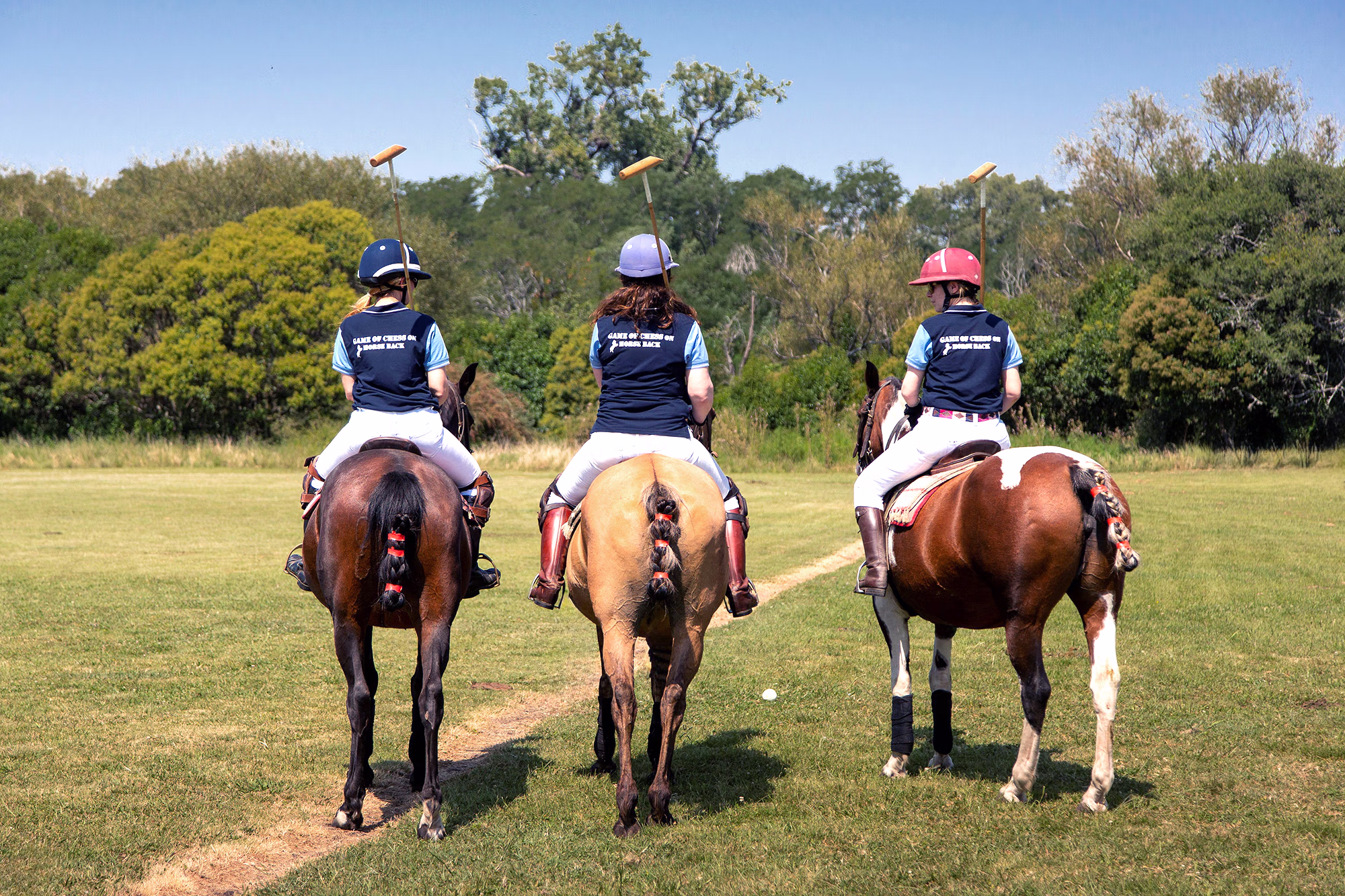 Trois joueurs de polo à cheval s’éloignent lentement de l’objectif, leurs maillets levés en l’air.