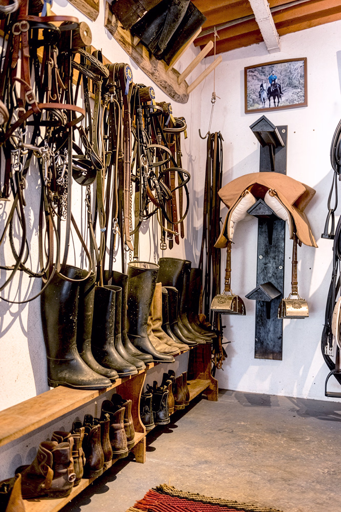 Une sellerie équestre bien rangée avec des longes suspendues au mur et des bottes d’équitation alignées sur un banc.