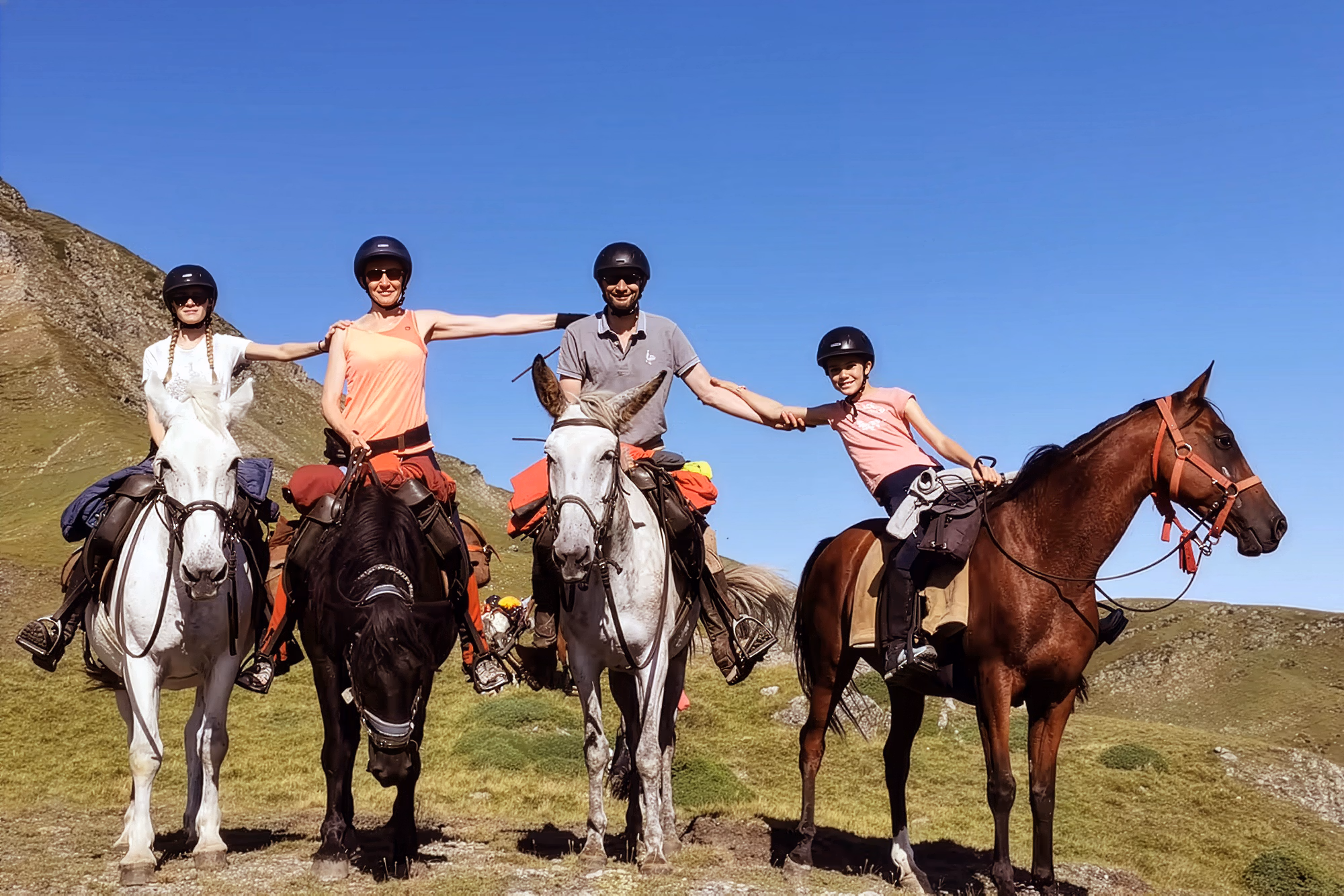 Quatre cavaliers souriants se tenant la main à cheval lors d’une randonnée équestre.