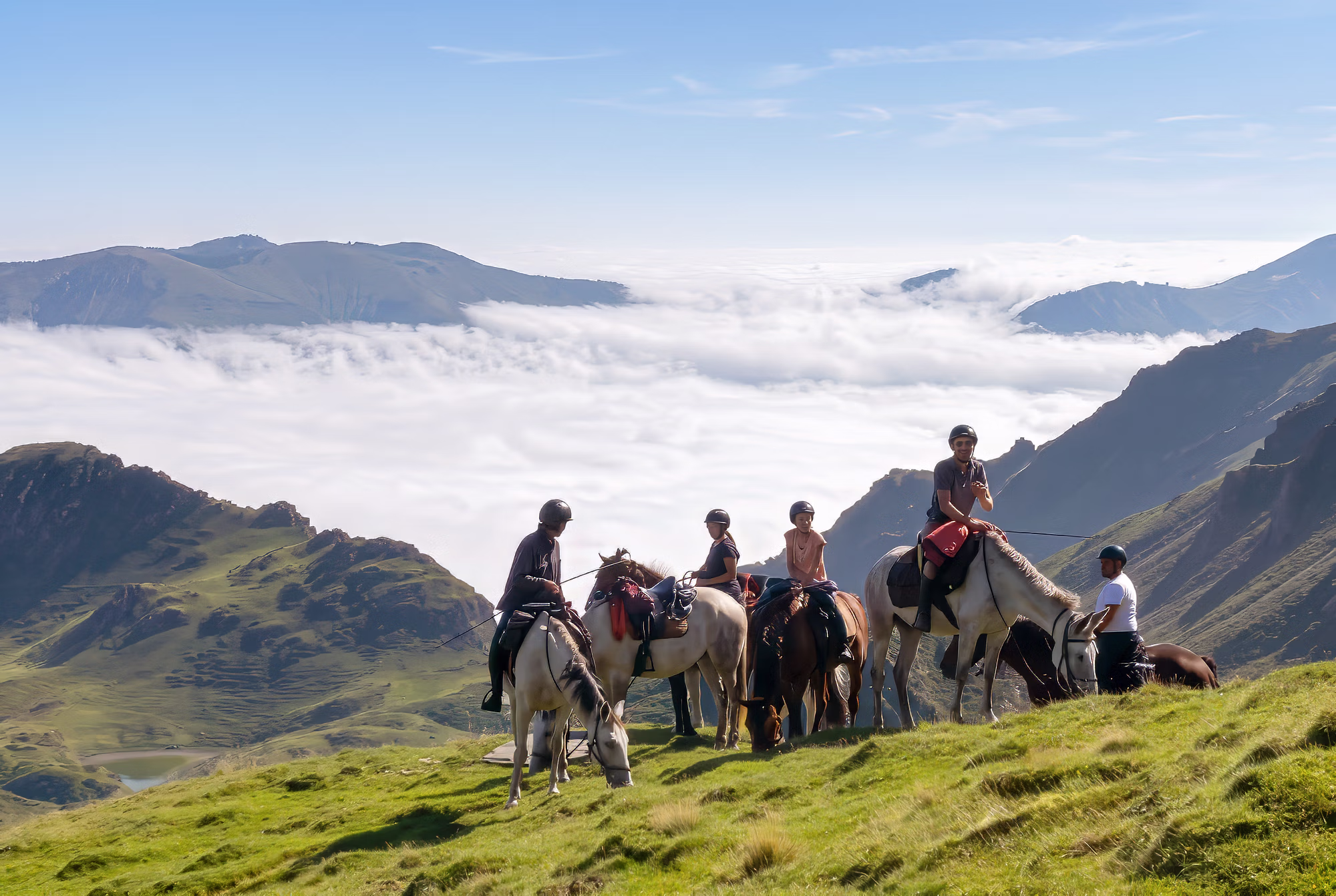 Un petit groupe de cavaliers au sommet d’une colline, avec les montagnes escarpées des Pyrénées, la brume et un beau ciel en arrière-plan.
